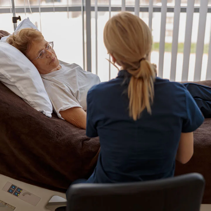 Victim advocate in teal scrubs comforts an older female in a hospital bed
