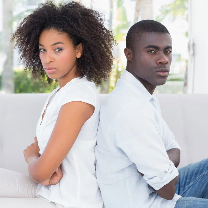 Portrait of young black couple, man and woman sitting back to back and looking serious as if in conflict