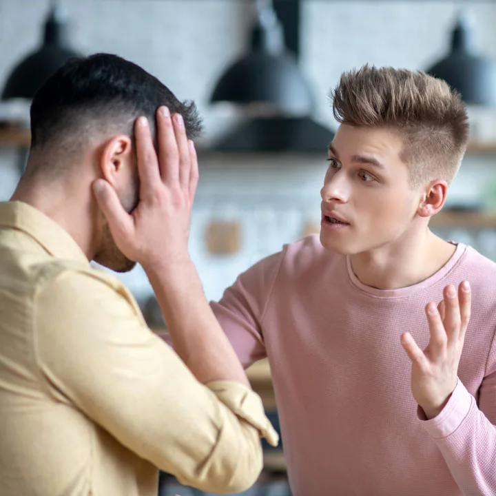 Gay male couple having an argument with dark-haired bearded man holding his head looking desperate