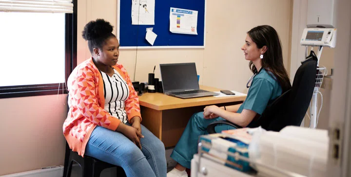 a sexual assault advocate in teal scrubs speaks with a young black female survivor