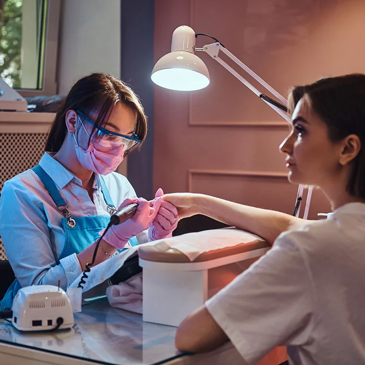 woman wearing a pink face mask working in a salon looks serious as she gives a manicure
