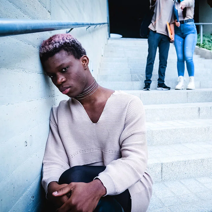 Upset African American transgender student leaning on wall