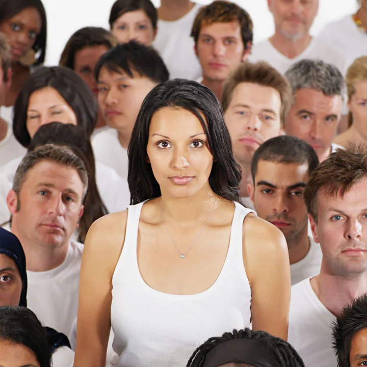 Portrait of young woman with light brown skin and dark hair wearing white, looking serious while surrounded by a diverse group of males also in white