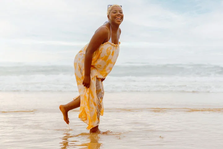 young curvy black girl in a summer dress laughing as she strolls by the sea 