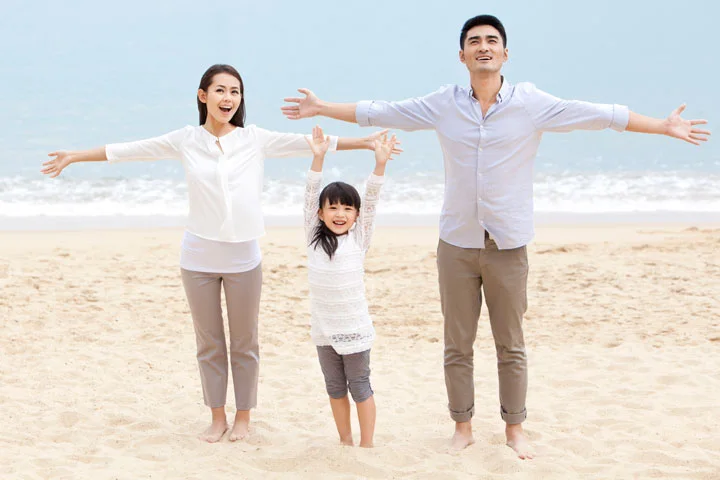 Happy young Chinese family, mom, dad, and daughter, having a good time on the beach