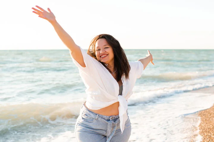 Happy adult woman 30-35 year old having fun over sea at beach outdoor