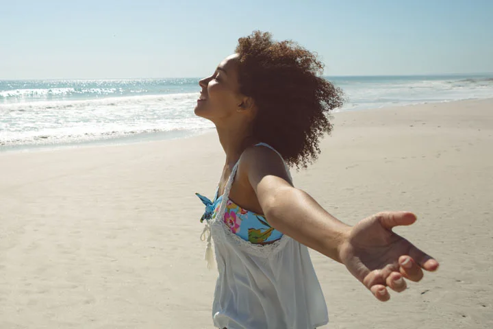 Side view of African american woman standing with arms outstretched on the beach