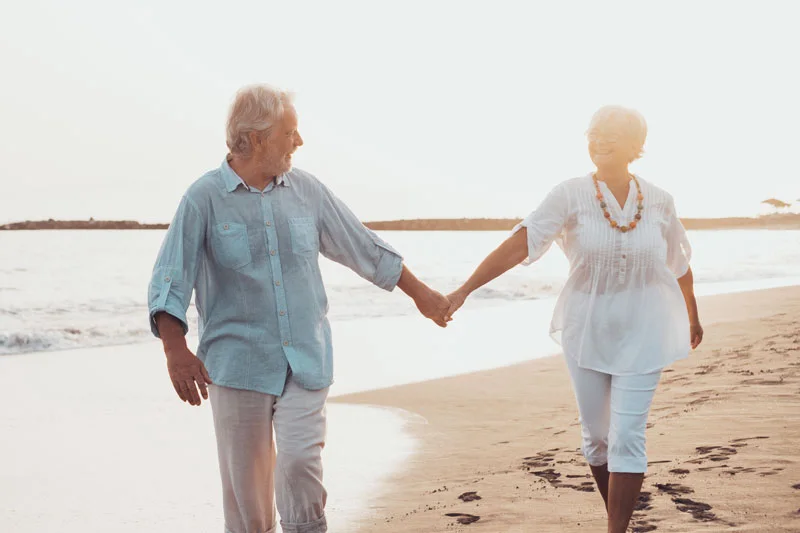 Couple of old mature people walking on the sand together and holding hands