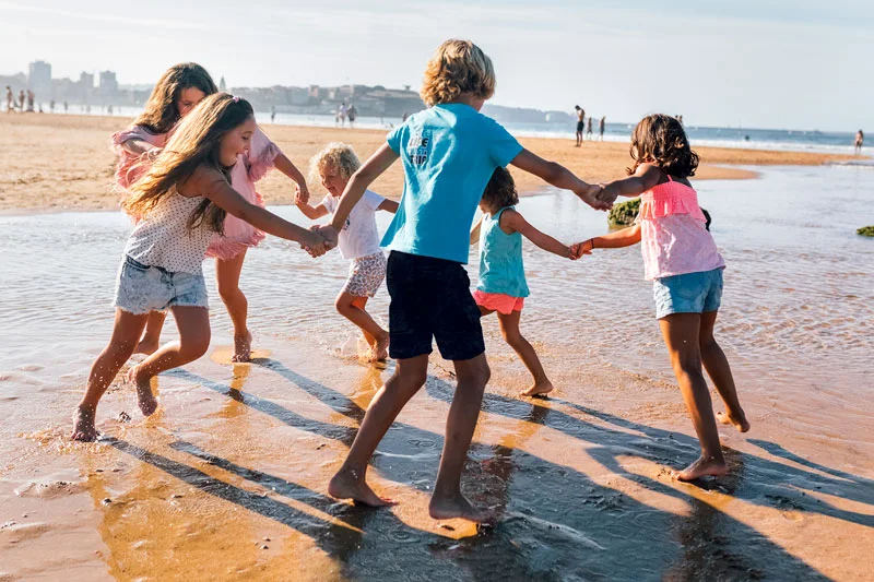 Group of six children playing, holding hands and dancing in a circle on the beach