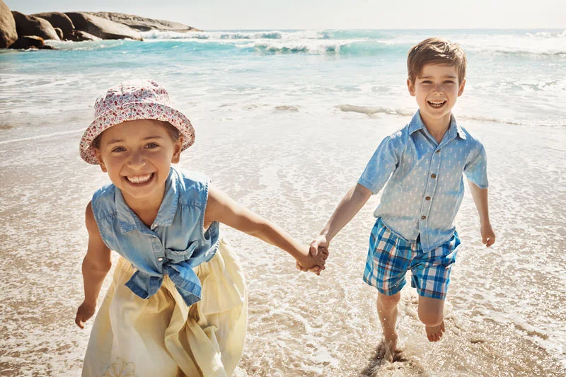Cute very young brother and sister smile widely while frolicking on the beach