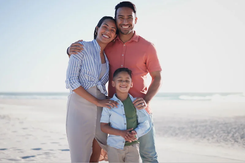 Attractive Latin mom and dad stand with their young son on the beach