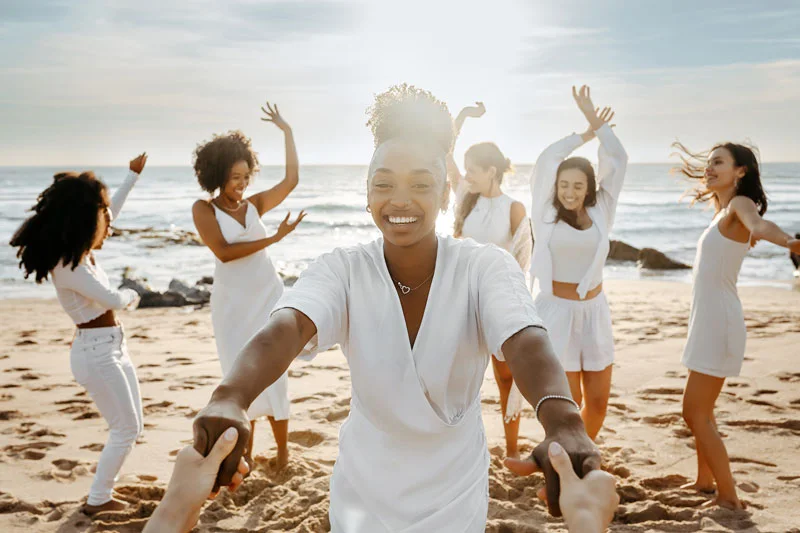 Diverse group of happy young female friends having fun and dancing outdoors on the beach