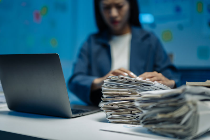 Young woman with a laptop goes through a stack of paperwork