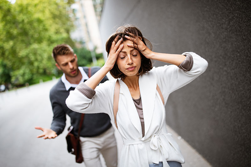 Young woman looks harried with her hands in her hair as she walks away from a male who is walking behind her, talking animatedly