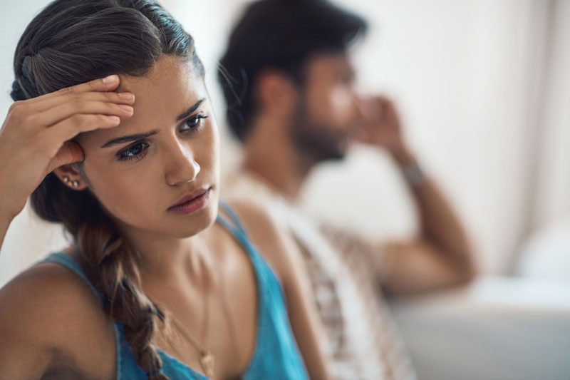 Young woman with braided brunette hair looks concerned as she sits with her back to a male figure