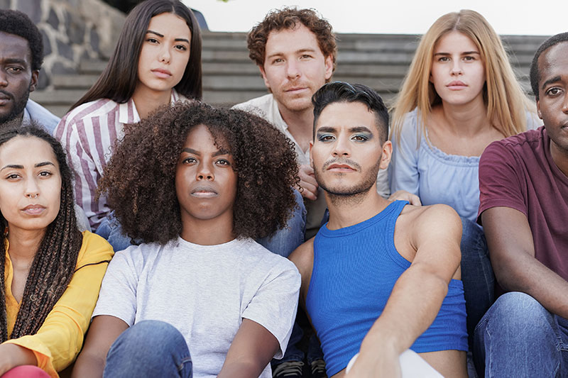 Diverse group of young people sitting in a group, looking seriously at the camera