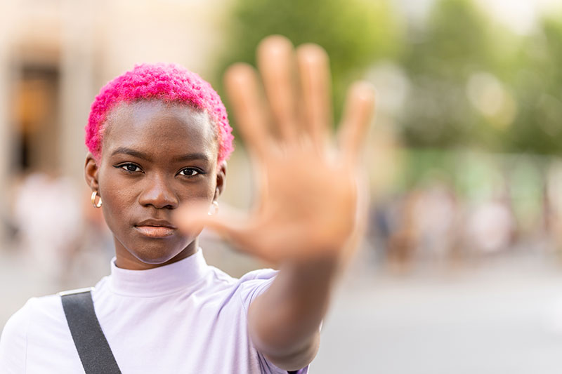 Young black woman with close-cropped, hot pink hair holds up her hand in a defiant stop gesture