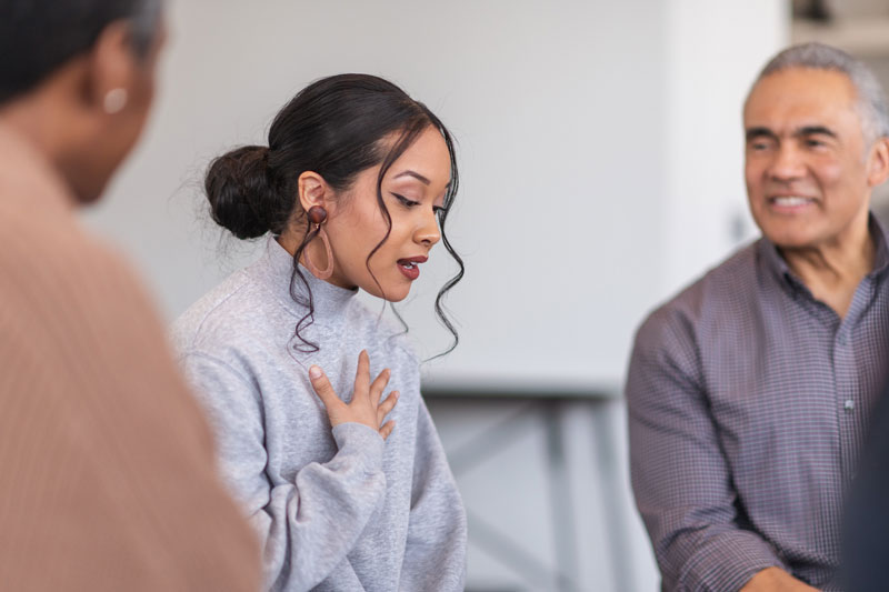 Young woman holds her hand to her heart and speaks earnestly at a support group meeting