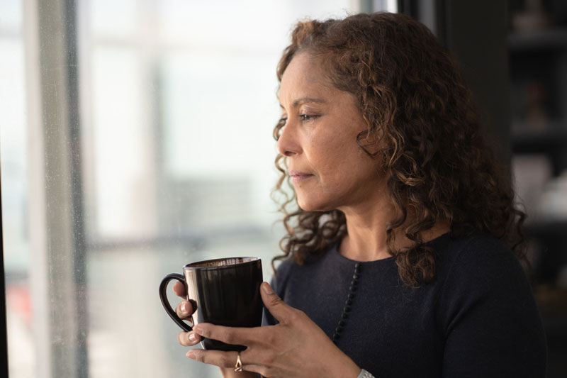 Mature adult black woman holds a cup of coffee and looks pensive and slightly sad